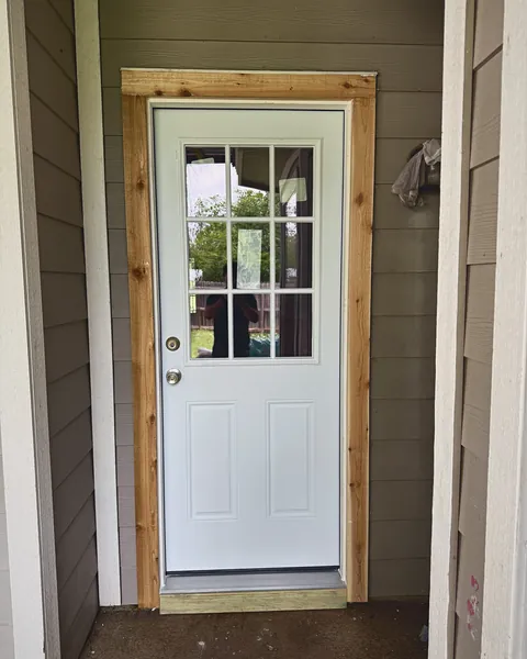 White nine-lite back door with new cedar casing under a covered porch