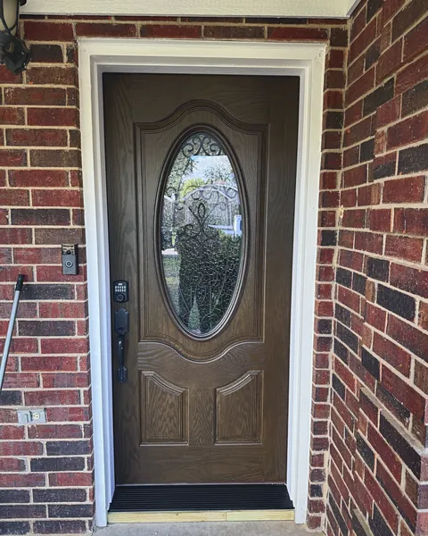 Stained entry door with decorative oval glass in a red brick entry
