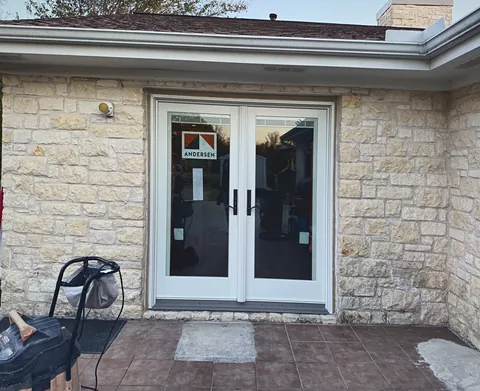New white Andersen French doors set in a limestone wall off a tiled patio