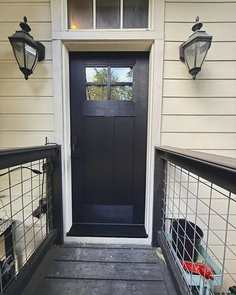 Black Craftsman entry door with transom window off a cable-rail deck