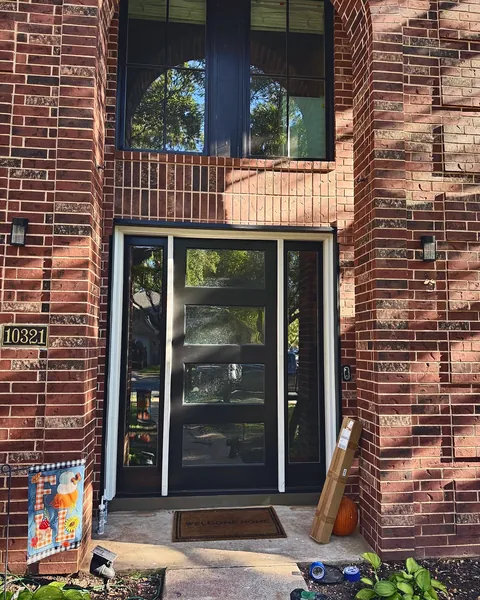 Black full-glass entry door with sidelights on a two-story brick home
