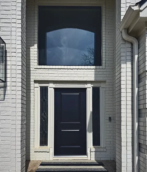 Black modern entry door with tall leaded-glass sidelights on a white brick home