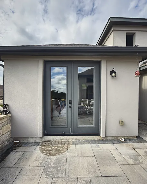 Gray full-glass French doors installed in a stucco wall off a paver patio