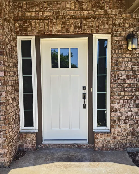 White Craftsman entry door with sidelights installed on a brick home