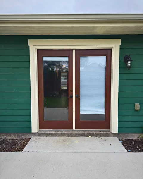 Wood-tone full-glass French doors with white trim on green siding
