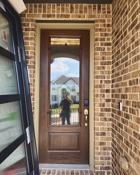Stained wood entry door with full-height arched glass in a brick entry